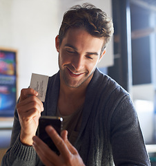 Image showing Business card, phone and young man in cafe dial mobile number for communication or call. Smile, contact paper and male person reading email or message on cellphone in coffee shop or restaurant.