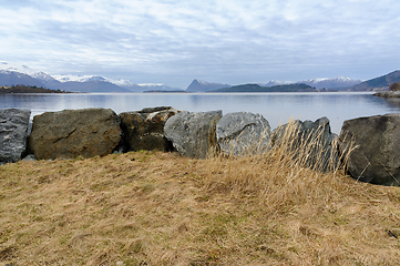 Image showing Tranquil scene showing the calm sea, boulders, and mountains under a soft evening sky.