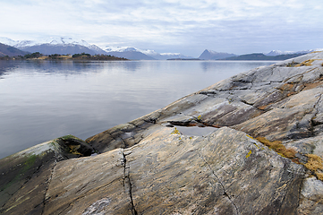 Image showing A tranquil seaside setting showing a rocky shore and distant snow-covered mountains under a soft evening sky.
