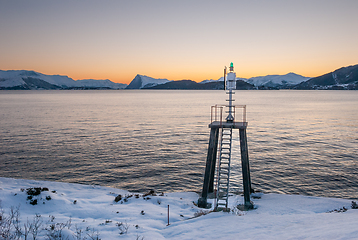 Image showing Snow-covered coastline with a navigation beacon overlooking a tranquil sea during a scenic sunset.