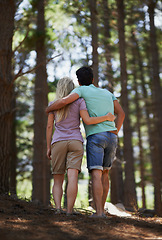 Image showing Couple, walking and hug in forest for love, embrace or support in trust, care or bonding in nature. Rear view or back of young man and woman in romance, affection or hiking together in outdoor woods