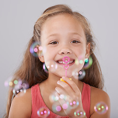 Image showing Portrait, kid and blowing bubbles in studio by toy, happiness and fun games for hand eye coordination. Little girl, face and learning to play on soap wand, development and sweet by gray background