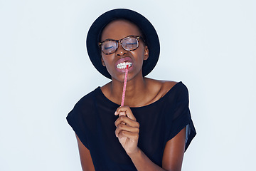 Image showing Face, fashion and black woman eating candy in studio on white background for sugar craving. Food, glasses and biting sweets with young african model eyes closed for appetite, greed or hunger