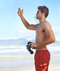 Image showing Man, binoculars and lifeguard on beach with whistle in security, emergency or health and safety. Young male person monitoring, bay watch or patrol by the ocean coast or sea in surveillance or danger