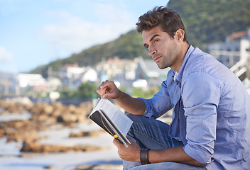 Image showing Beach, book and young man reading for knowledge or relaxing hobby on vacation or holiday. Travel, outdoor and handsome confident male person enjoying story or novel on weekend trip or adventure.