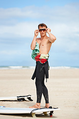 Image showing Surfing, man and getting ready with sunglasses on beach with wetsuit, blue sky or surfboard with mock up space. Extreme sports, athlete and person by ocean for training, surfer workout or confidence