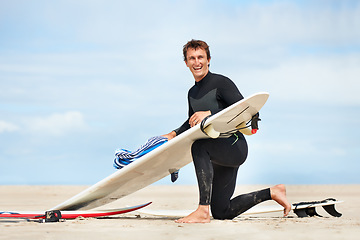 Image showing Surfer, man and portrait with surfboard on beach with wetsuit, blue sky and cleaning with mock up space. Extreme sports, athlete and person by ocean for training, surfing workout and towel with smile