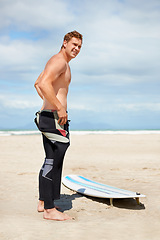 Image showing Surfer, man and wetsuit with surfboard on beach with getting ready, blue sky and dressing with mock up space. Face, athlete and person by ocean for training, surfing workout and extreme sports