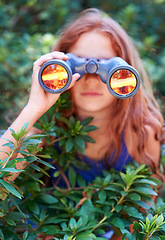Image showing Girl, kid with binoculars and search in nature for learning and fun, forest and adventure at summer camp. Young camper, leaves and explore environment outdoor in bush with hiking and discovery
