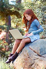 Image showing Young girl, forest and laptop on rock for internet, break and connection on holiday in woods for travel tips. Child, red hair and computer on boulder for online research, camping and relax by trees