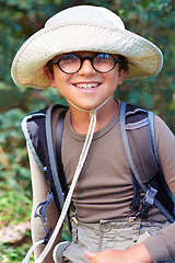 Image showing Boy, kid and hiking in nature, portrait with glasses and scout outdoor for adventure, travel and fun with backpack. Discover, exploring and summer camp with happy camper in park, youth and recreation