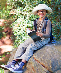 Image showing Boy, kid and hiking, relax on rock and book for reading, backpacking and adventure outdoor. Student on school field trip, nature and forest for discovery and exploration, smile in portrait and travel