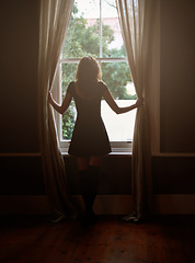 Image showing Woman, curtain and morning by window for sunlight, vitamin D or sunshine in bedroom at home. Rear view of female person standing by blinds or glass in casual clothing and looking out in neighborhood