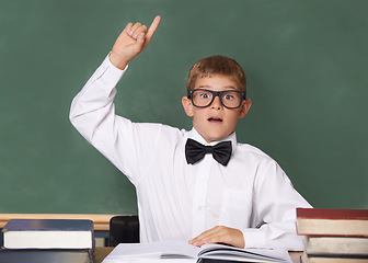 Image showing Young boy, portrait and question at school for learning, education or interaction for knowledge by green chalk board. Face of male person, smart child or teenager with books and hand raised in class