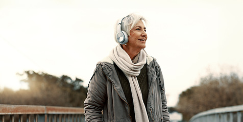 Image showing Senior woman, headphones and music outdoor, walking and wellness with audio streaming and energy. Podcast, listen to radio and sound with female person on city bridge, exercise and travel with tech