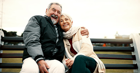 Image showing Hug, bench and senior couple on bench at park with love to relax with quality time or care. Retirement, support and elderly man or woman in nature with embrace or laugh in outdoor with bonding.