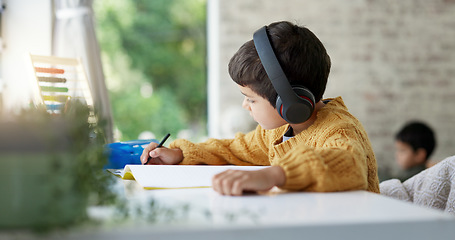 Image showing Boy child, homework and writing with headphones, music and focus for learning, drawing or education. Young male kid, notebook and study with audio streaming, radio or listening online in family house