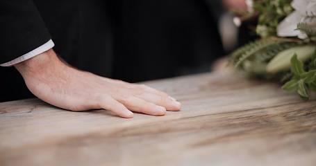 Image showing Death, funeral and hand of man on coffin, family at service in graveyard or church for respect. Flowers, loss and people at wood casket in cemetery with memory, grief and sadness at grave for burial.