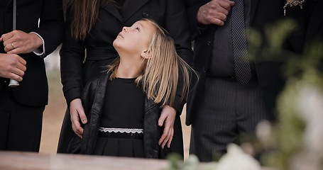 Image showing Mourning, grief and family with girl at funeral, flowers on coffin, death and sad child at service in graveyard. Support, loss and people at casket in cemetery with kid crying at grave for burial.