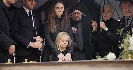 Image showing Loss, grief and people at funeral with umbrella, flowers and coffin, family with sad child at service in graveyard. Roses, death and group in rain at casket in cemetery with kid at grave for burial.