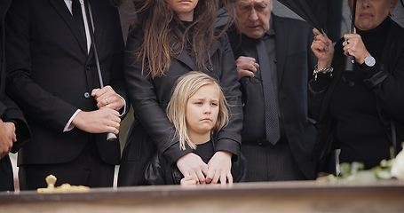 Image showing Loss, grief and people at funeral with umbrella, flowers and coffin, family with sad child at service in graveyard. Roses, death and group in rain at casket in cemetery with kid at grave for burial.