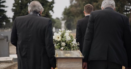 Image showing Men, coffin and pallbearers walking at cemetery ceremony outdoor at burial tomb. Death, grief and group casket at funeral, carry to graveyard and family service of people mourning at windy event.