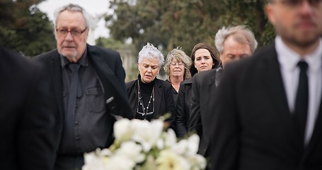 Image showing Pallbearers, men and walking with coffin in funeral, ceremony or mourning event at graveyard with sad, grief and flowers. People, support and walk with family in memorial service together with casket