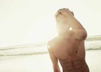 Image showing Man, shirtless and relaxing on beach at sunset, confidence and tourist at sea on summer holiday. Male person, lens flare and outdoor adventure for fun, calm ocean and peaceful environment in nature