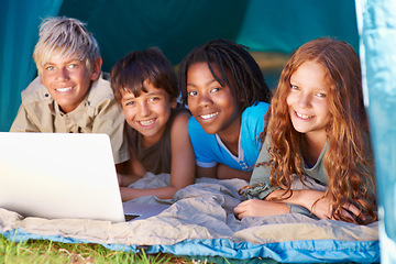 Image showing Children, portrait and happy with laptop for camping in tent, social media or online movie with diversity in nature. Friends, face and group with smile outdoor on grass for trip, relax or holiday fun