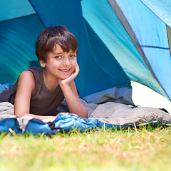 Image showing Boy, child and camping, relax in tent and summer vacation with travel and happy in portrait outdoor. Rest on sleeping bag, young camper with smile and adventure in nature, childhood and recreation