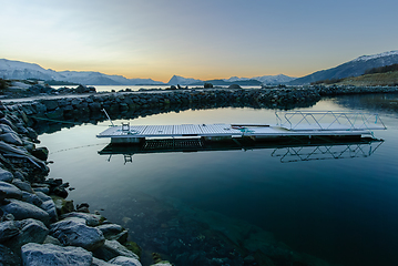Image showing A tranquil scene as the sun sets behind snow-covered mountains, reflecting off the placid sea.