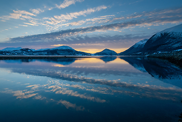 Image showing Sunset colors paint the sky as the calm lake mirrors the mountains and clouds at dusk.