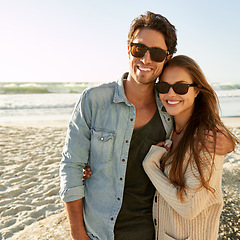 Image showing Couple, beach and sunglasses with hug, happy or care with fashion, eye protection or vacation in summer. Man, woman and embrace with glasses for sun, trendy style or love by waves on tropical holiday