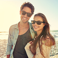 Image showing Couple, ocean and sunglasses with hug, smile or care for fashion, eye protection or vacation in summer. Man, woman and embrace in glasses at beach for sun, happy or love by waves on tropical holiday