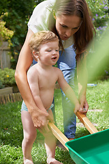 Image showing Mother, boy and toddler with a wheelbarrow in garden, nature or grass for playing and fun in summer. Walking, backyard or kid with family, child development and mom with smile, growth and happiness