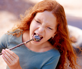 Image showing Girl, marshmallow and eating in nature, camping holiday and fire for roast snack in forest. Red hair, teenager and hungry for chocolate candy with happiness and outdoor vacation in woods for kids