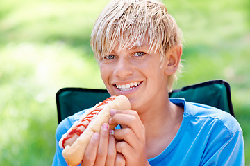 Image showing Child, eating and portrait with hotdog outdoor in camping chair and relax at barbecue with lunch. Happy, kid and hungry for food from bbq in park, woods or forest on holiday or vacation in summer