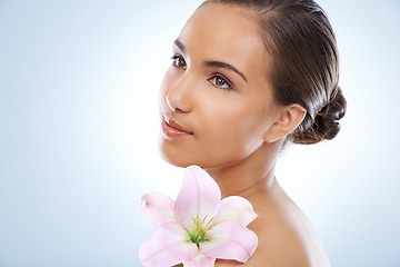 Image showing Woman, face and flower in natural skincare, beauty or cosmetics on a blue studio background. Young female person smile with plant or petals on shoulder for glow, care or smooth skin on mockup space