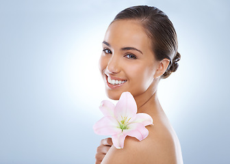 Image showing Happy woman, portrait and flower in natural skincare, beauty or cosmetics on a blue studio background. Face of young female person smile with plant on shoulder for nature or glow on mockup space