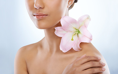 Image showing Woman, hand and flower in natural skincare, beauty or cosmetics on a blue studio background. Closeup of young female person with plant, petals or bloom on shoulder for nature, glow or cosmetology