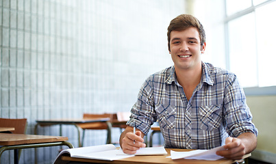 Image showing Student, man and portrait in classroom for education, learning and writing of knowledge in university. Face of young and smart person with notes for college research, essay paper and studying at desk
