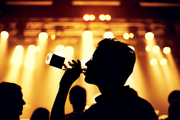 Image showing Night, club and man with a drink at party, event or music festival with stage lights and silhouette. Dark, concert and person dance with bottle of alcohol in crowd at social celebration or rave