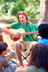 Image showing Nature, camp and man playing guitar for entertainment, talent or music in woods or forest. Singing, musician and male person with acoustic string instrument outdoor in park or field on weekend trip.