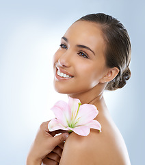 Image showing Happy woman, face and flower in natural skincare, beauty or cosmetics on a blue studio background. Young female person smile with plant or petals on shoulder for glow, care or smooth skin on mockup