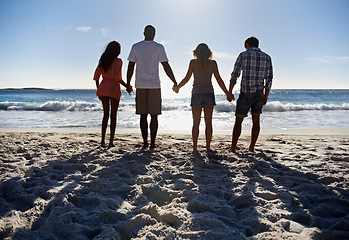 Image showing Holding hands, ocean or group of friends walking at sea on holiday vacation together in summer. Support, people or back of men with women or love to relax on beach, sand or nature for travel or break