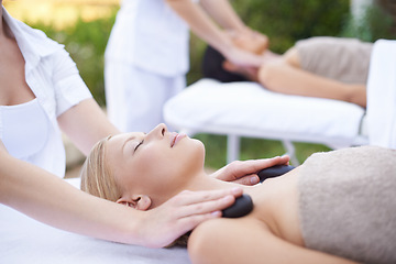 Image showing Women, hands and massage with hot stone in spa, outdoor and wellness on bed for body treatment. People, heat and masseuse for release of muscle tension, nature and health detox in comfort at resort