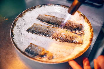 Image showing Chef cooks fish using gas burner torch.