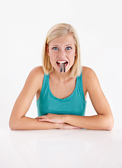 Image showing Woman, portrait and eating a fish, tail or strange food in mouth on white background of studio. Crazy, diet and person with weird seafood, cuisine and face of disgust for taste of tuna or salmon