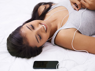 Image showing Woman, relax on bed and listening to music on phone with smile for podcast, sound and streaming service at home. Young person with mobile app for audio, happy song and dream or sleeping in bedroom