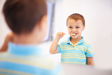 Image showing Boy child, brushing teeth and mirror in bathroom for cleaning, hygiene or health for routine in home. Kid, toothbrush or reflection for dental wellness, smile or results in morning at family house